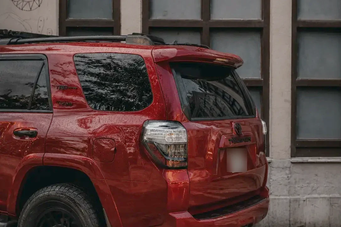 A red Toyota 4Runner parked on wet pavers, rain still beaded across the tailgate and rear glass.
